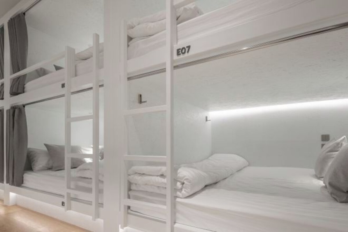 A bunk bed room with white bedding and a ladder.