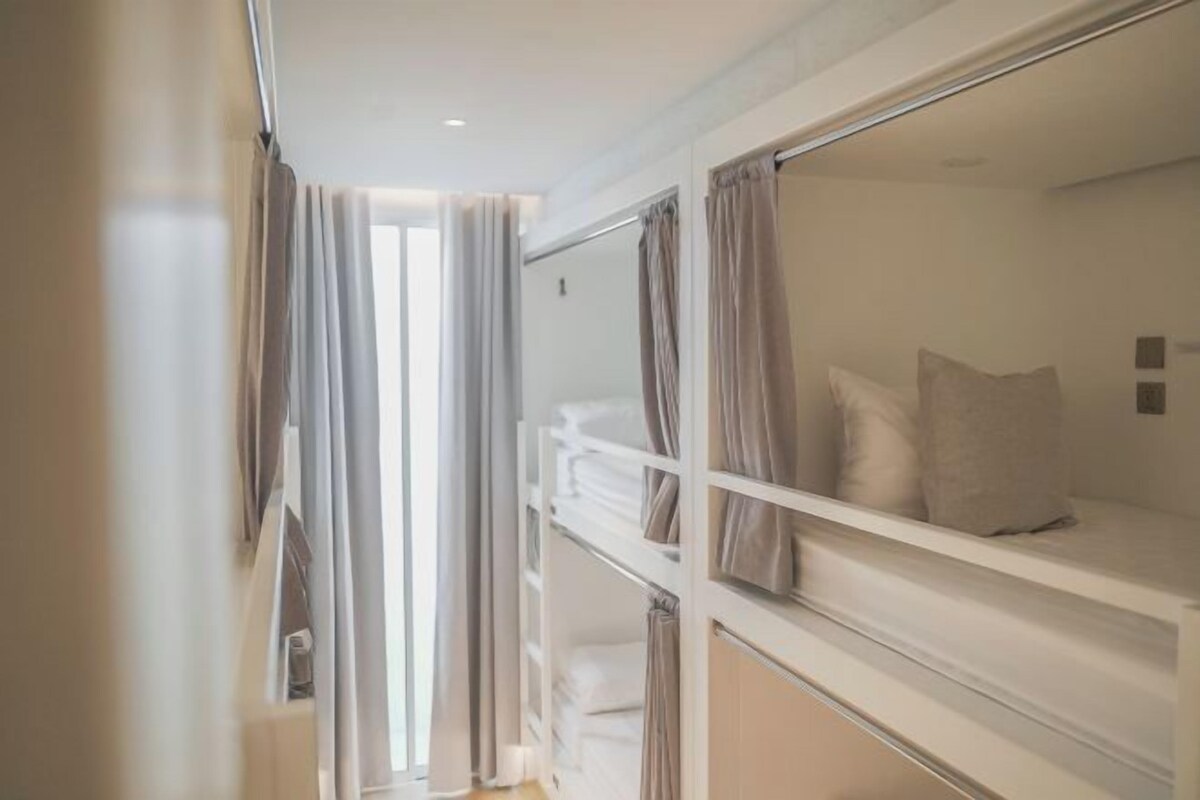 A hotel room with a bunk bed, a wardrobe, and a window with curtains.