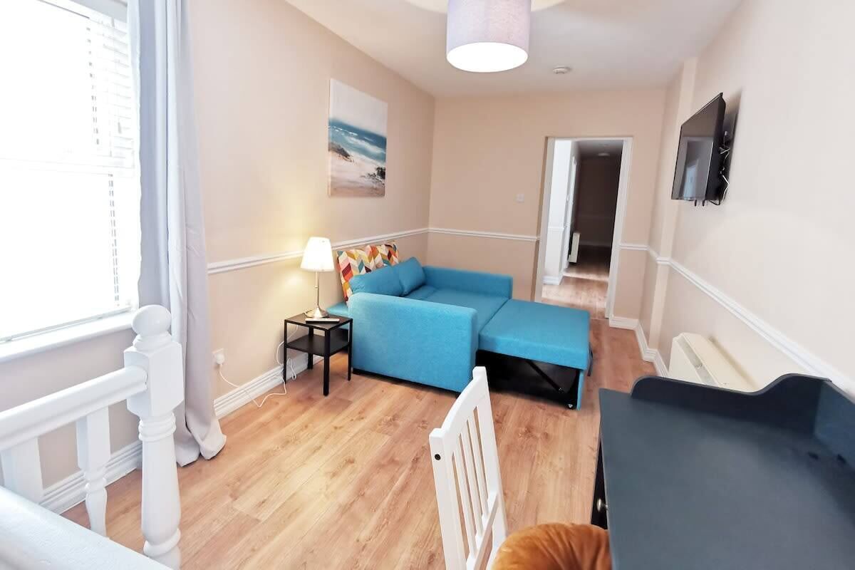 Un salon moderne avec un canapé bleu, une petite table avec une lampe et un téléviseur fixé au mur.