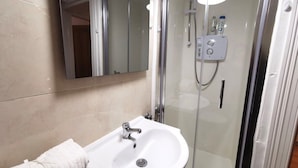 Een badkamer met een wit wastafelmeubel, een douchecabine van glas en een spiegel boven het wastafelmeubel.