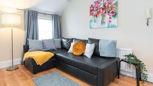 Een moderne woonkamer met een zwarte leren bank, een vloerlamp, een bloemschilderij en een radiator.