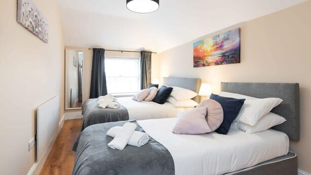 Een hotelkamer met twee bedden, een groot raam met gordijnen, een schilderij aan de muur en een plafondlamp.
