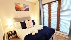 Una camera d'albergo con un letto, un comodino, una lampada, un quadro appeso al muro e una finestra con persiane.