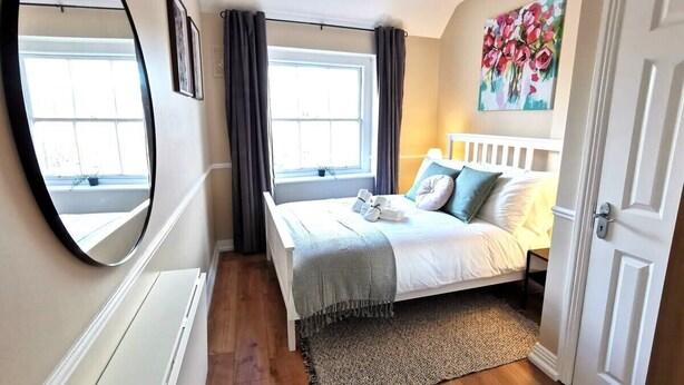 Ein Schlafzimmer mit Bett, Fenster, Heizkörper, Spiegel, Tür und einem Gemälde an der Wand.