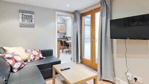 A modern living room with a sofa, a coffee table, a flat-screen TV, and a kitchen area visible through an open door. - Great House Trendy Ranelagh 3bed 2bath TV and WIFI (Dublin 6)