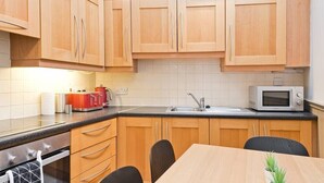 A compact kitchen with wooden cabinets, a microwave, a sink, and a dining area with chairs. - Great House Trendy Ranelagh 3bed 2bath TV and WIFI (Dublin 6)