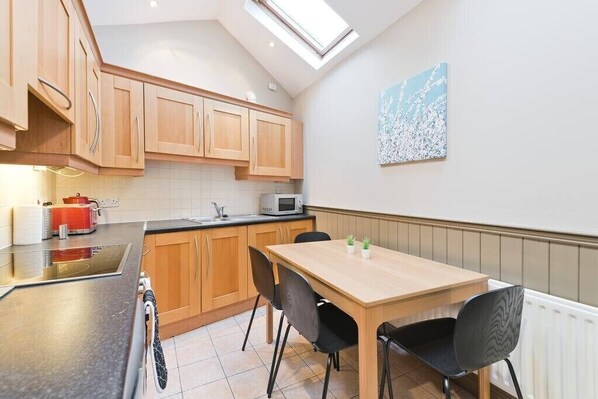 A kitchen with wooden cabinets, a microwave, a table with chairs, and a skylight. - Great House Trendy Ranelagh 3bed 2bath TV and WIFI (Dublin 6)