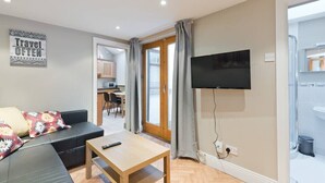 A modern living room with a sofa, a coffee table, a flat-screen TV mounted on the wall, and a sliding glass door leading to a kitchen. - Great House Trendy Ranelagh 3bed 2bath TV and WIFI (Dublin 6)