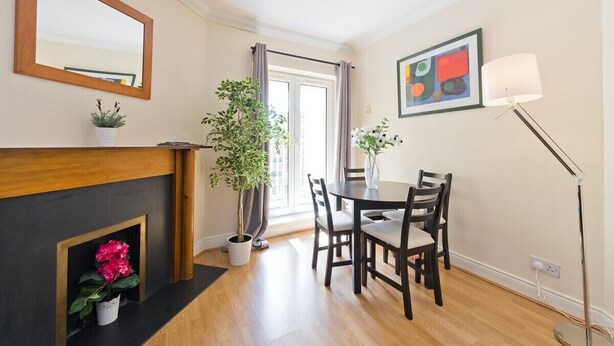 Een moderne woonkamer met een open haard, een eettafel met stoelen, een grote spiegel en een vloerlamp.