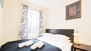 Een hotelkamer met een bed, nachtkastje, ingelijst kunstwerk en raam met gordijnen.