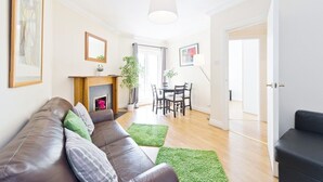 Een moderne woonkamer met een leren bank, groene tapijten, een open haard en een eethoek met een tafel en stoelen.