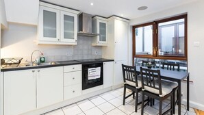 A modern kitchen with white cabinets, a black countertop, and a built-in oven. There is a dining area with a table and chairs. - GREAT NEIGHBORHOOD SUPER 2 bed COTTAGE SUIT FAMILY (Dublin 8)