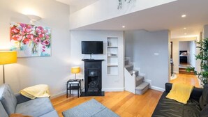 A modern living room with a fireplace, a flat-screen TV, and a staircase leading to another level. - GREAT NEIGHBORHOOD SUPER 2 bed COTTAGE SUIT FAMILY (Dublin 8)