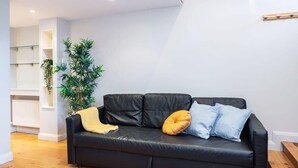 A modern living room with a black leather sofa, a yellow throw blanket, and a large green plant. - GREAT NEIGHBORHOOD SUPER 2 bed COTTAGE SUIT FAMILY (Dublin 8)