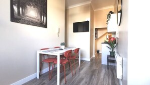 A dining area with a white table and red chairs, a painting on the wall, a flat-screen TV, and a staircase leading to another level. - Cosy Apartment near OConnell St Reliable Fast WIFI (Dublin 1)