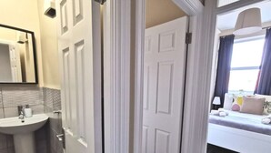 A hotel room with a white door, a bathroom with a sink and mirror, and a bed with pillows and a lamp. - Cosy Apartment near OConnell St Reliable Fast WIFI (Dublin 1)