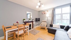 Ein Wohnzimmer mit Esstisch, Stühlen, einer Couch, einem Fernseher und einem Kamin.