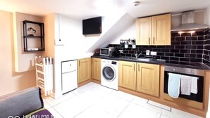 A compact kitchen with wooden cabinets, a washing machine, a microwave, and a built-in oven. - Good location Cosy flat Ranelagh (Dublin 6)