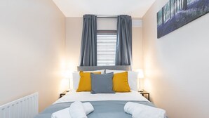 A neatly made bed with white and gray linens, two pillows, and two rolled towels on the bed. - Great City CENTRE LOCATION SPACIOUS 2 BED APT (Dublin 1)
