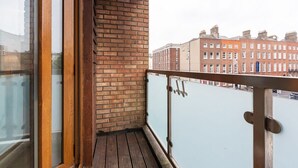 A balcony with a wooden floor, brick wall, and a glass railing overlooking a river and buildings. - Great City CENTRE LOCATION SPACIOUS 2 BED APT (Dublin 1)
