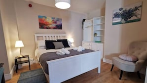 A bedroom with a bed, bedside tables, a chair, a shelf, and artwork on the walls. - Central Apartment Private patio reliable fast WIFI (Dublin 1)