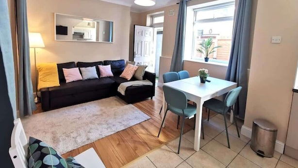 A living room with a sofa, a dining table with chairs, a lamp, and a window with curtains. - Central Apartment Private patio reliable fast WIFI (Dublin 1)