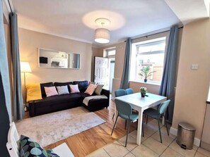 A living room with a sofa, a dining table with chairs, a lamp, and a window with curtains. - Central Apartment Private patio reliable fast WIFI (Dublin 1)