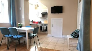 A dining area with a table and chairs, a kitchen in the background, and a television mounted on the wall. - Central Apartment Private patio reliable fast WIFI (Dublin 1)