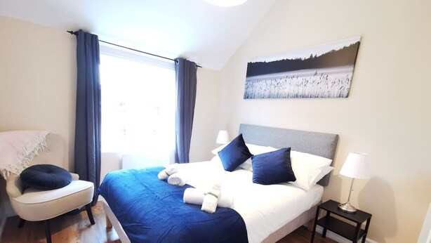 A bedroom with a bed, a chair, a nightstand, a lamp, and a painting on the wall. - Great new 2bed apartment in city centre*fast WIFI (Dublin 1)