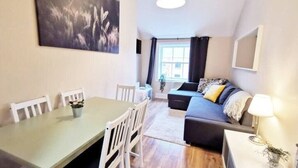 A modern living room with a sofa, a dining table with chairs, a large window with curtains, and a painting on the wall. - Great new 2bed apartment in city centre*fast WIFI (Dublin 1)
