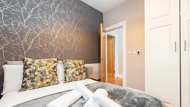 Ein modernes Hotelzimmer mit einem großen Bett, dekorativen Kissen, einem Marmorkopfschild und Blick auf den Flur.