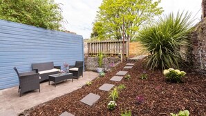 Eine Terrasse mit Gartenmöbeln, einem Kiesweg und verschiedenen Pflanzen.