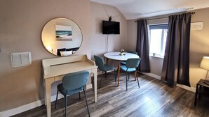 Une pièce avec un grand miroir rond, un téléviseur, une petite table avec des chaises, une fenêtre avec des rideaux et une lampe.