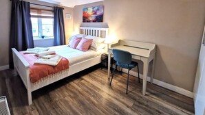 Une chambre à coucher avec un lit, un bureau, une chaise, une fenêtre avec des rideaux, un tableau au mur et un luminaire au plafond.