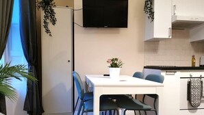 Eine moderne Küche mit Flachbildfernseher, weißen Schränken und einem Essbereich mit weißem Tisch und blauen Stühlen.