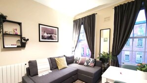 Ein modernes Wohnzimmer mit einer grauen Eckcouch, einem weißen Tisch und einem großen Fenster mit Vorhängen.