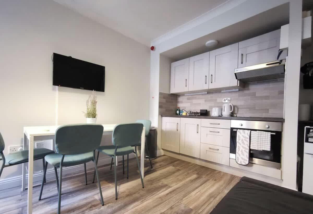 A compact kitchen with a dining area, a flat-screen TV, and a small potted plant.