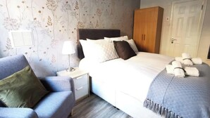 Een slaapkamer met een bed, nachtkastje, lamp en een kledingkast.