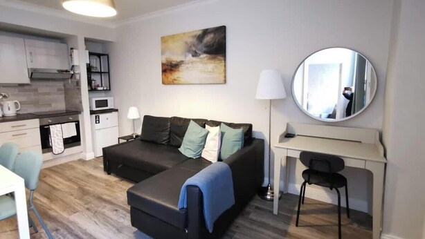 Een moderne woonkamer met een bank, een bureau, een spiegel en een keukenhoek.