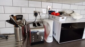 Et køkken med en brødrister, kaffemaskine og mikroovn. Der er en redskabsholder med forskellige køkkenredskaber.