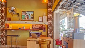 Een restaurantinterieur met een toonbank, barstoelen, een tafel, stoelen, een ventilator, een ingelijst kunstwerk en een menubord.