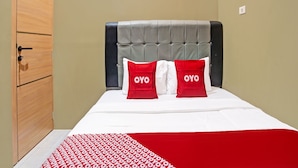 Een hotelkamer met een bed, een houten kledingkast en een grijs gestoffeerd hoofdeinde.