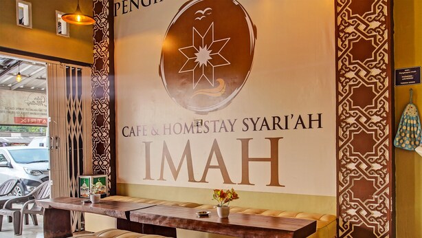 Een receptiegedeelte met een houten balie, een comfortabele bank en een muur met de tekst 'Café & Homes Stay Syari'ah IMAH'.
