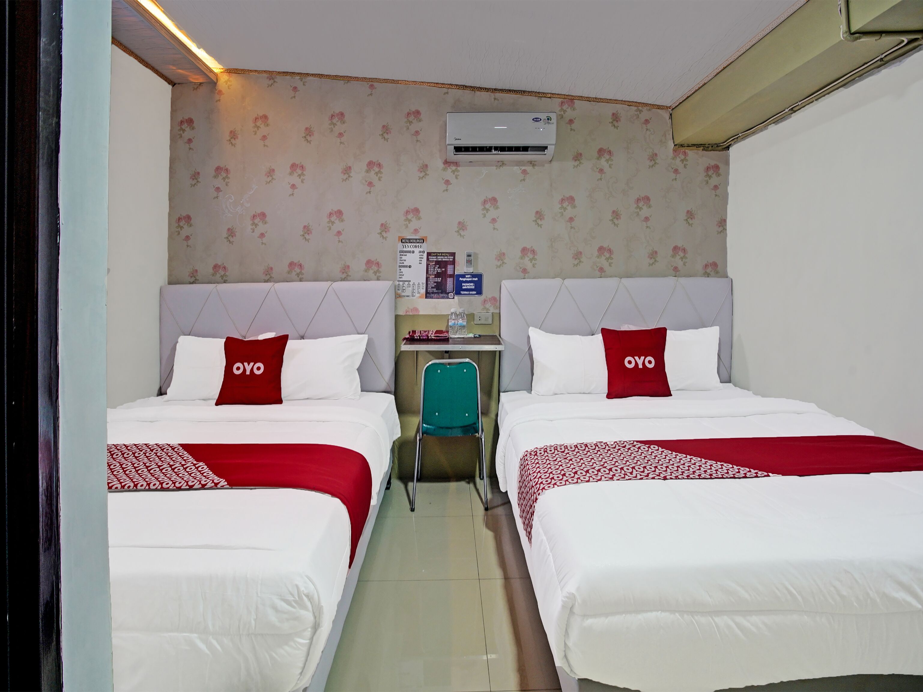 Une chambre d’hôtel avec deux lits, chacun agrémenté d’un oreiller rouge et blanc portant l’inscription « OYO », une petite table avec une bouteille d’eau et un climatiseur fixé au mur.