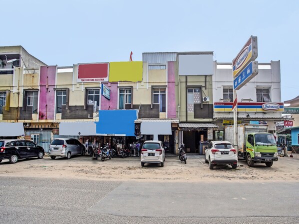 Un immeuble à plusieurs étages dont le rez-de-chaussée abrite divers commerces, notamment un distributeur automatique de billets et un magasin appelé « Indomaret ».