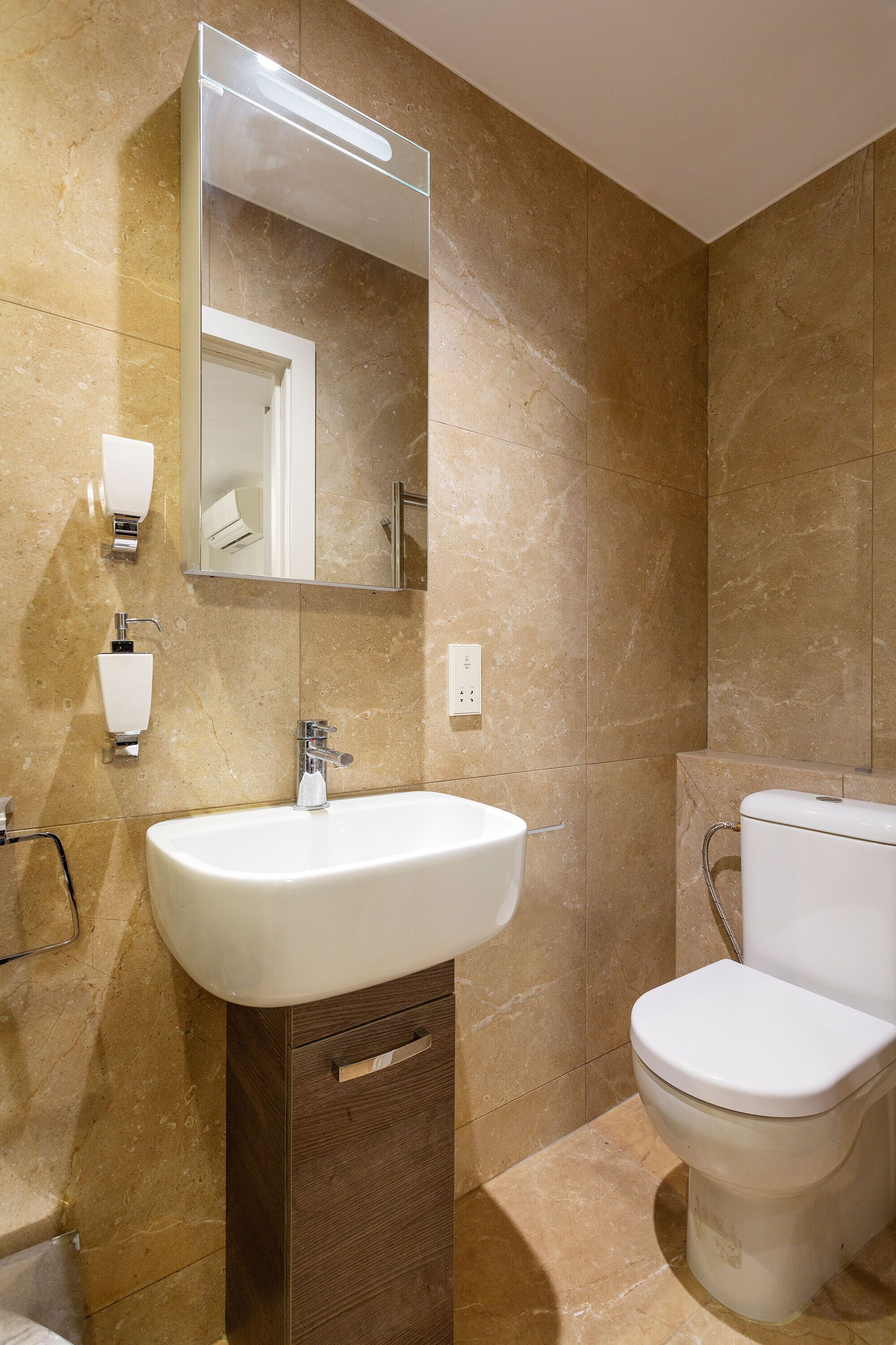 A bathroom with a sink, mirror, toilet, and marble walls.