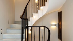 Una escalera en espiral moderna con escalones blancos y barandillas negras, iluminada por luces fijadas a la pared.