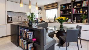 Una cocina moderna con una zona de estar integrada, una mesa de comedor de cristal y una estantería llena de libros.