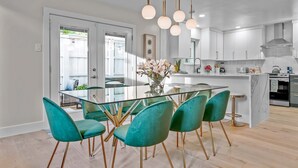 A modern kitchen with a glass dining table, teal chairs, and pendant lighting.