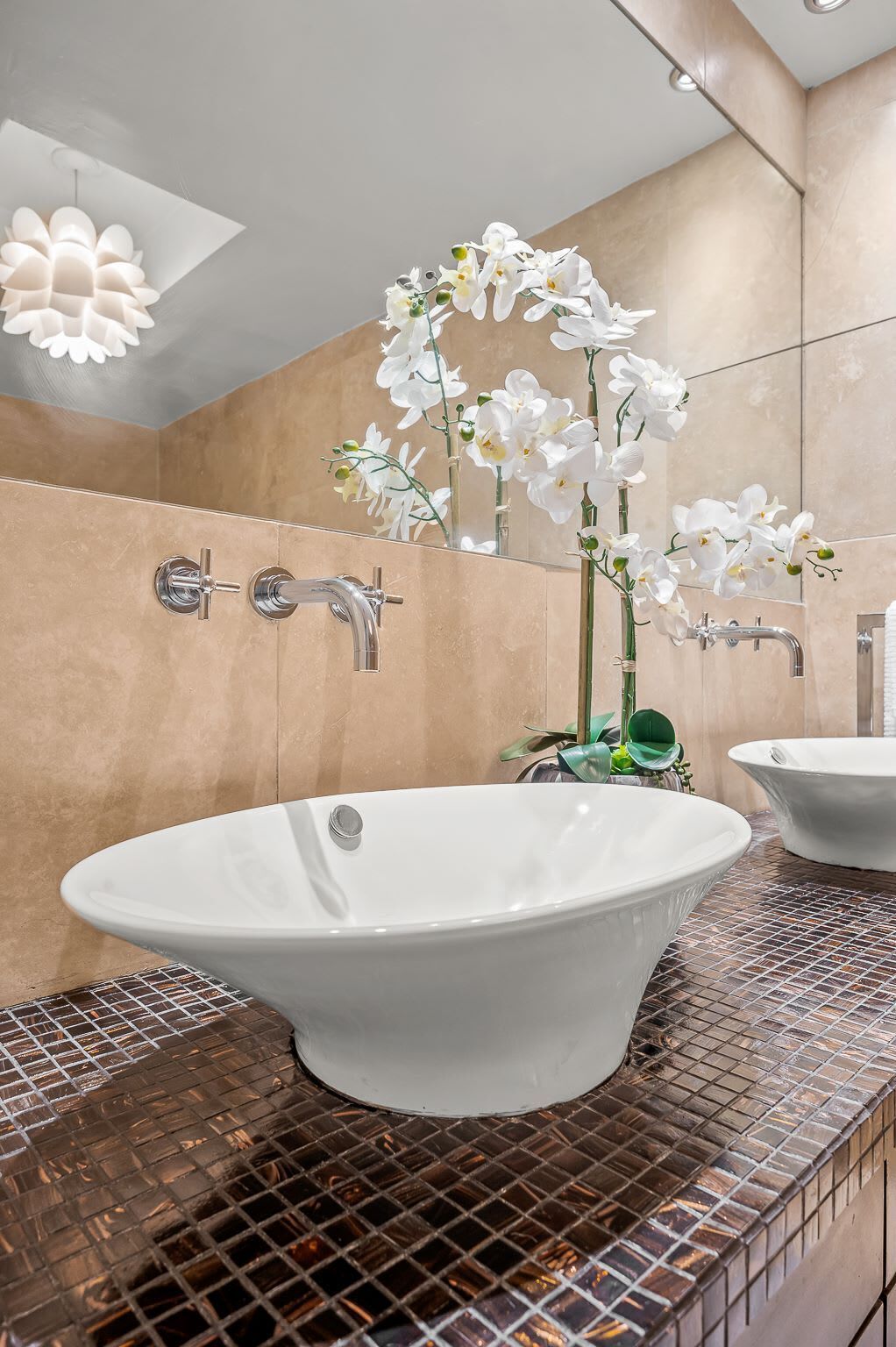 Un baño con una bañera independiente, un espejo y orquídeas blancas.